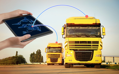 Image of Logistics concept. Woman using tablet with world map on screen against trucks