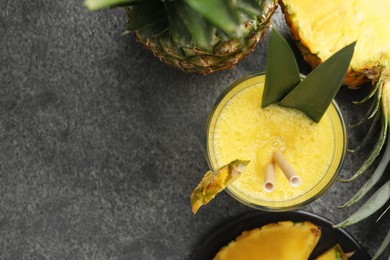 Photo of Tasty pineapple smoothie and fruit on grey table, flat lay. Space for text