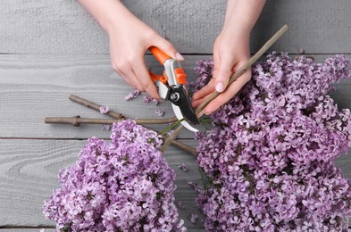 Photo of Woman trimming lilac branches with secateurs at wooden table, top view