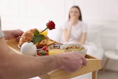 Photo of Romantic breakfast. Husband bringing tray with tasty food to his wife in bedroom, closeup