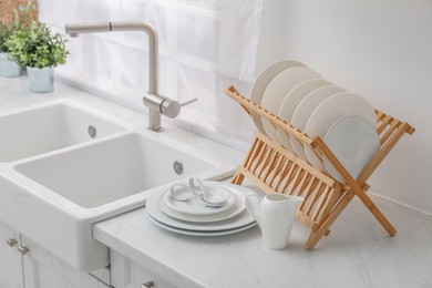 Photo of Drying rack with clean dishes on light marble countertop near sink in kitchen