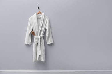 Photo of Fresh white bathrobe hanging on light wall. Space for text