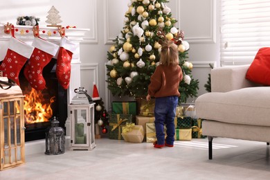 Photo of Cute little girl near Christmas tree at home, back view