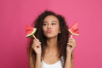 Beautiful young African American woman with pieces of watermelon on crimson background