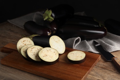 Photo of Cut and whole raw ripe eggplants on wooden table