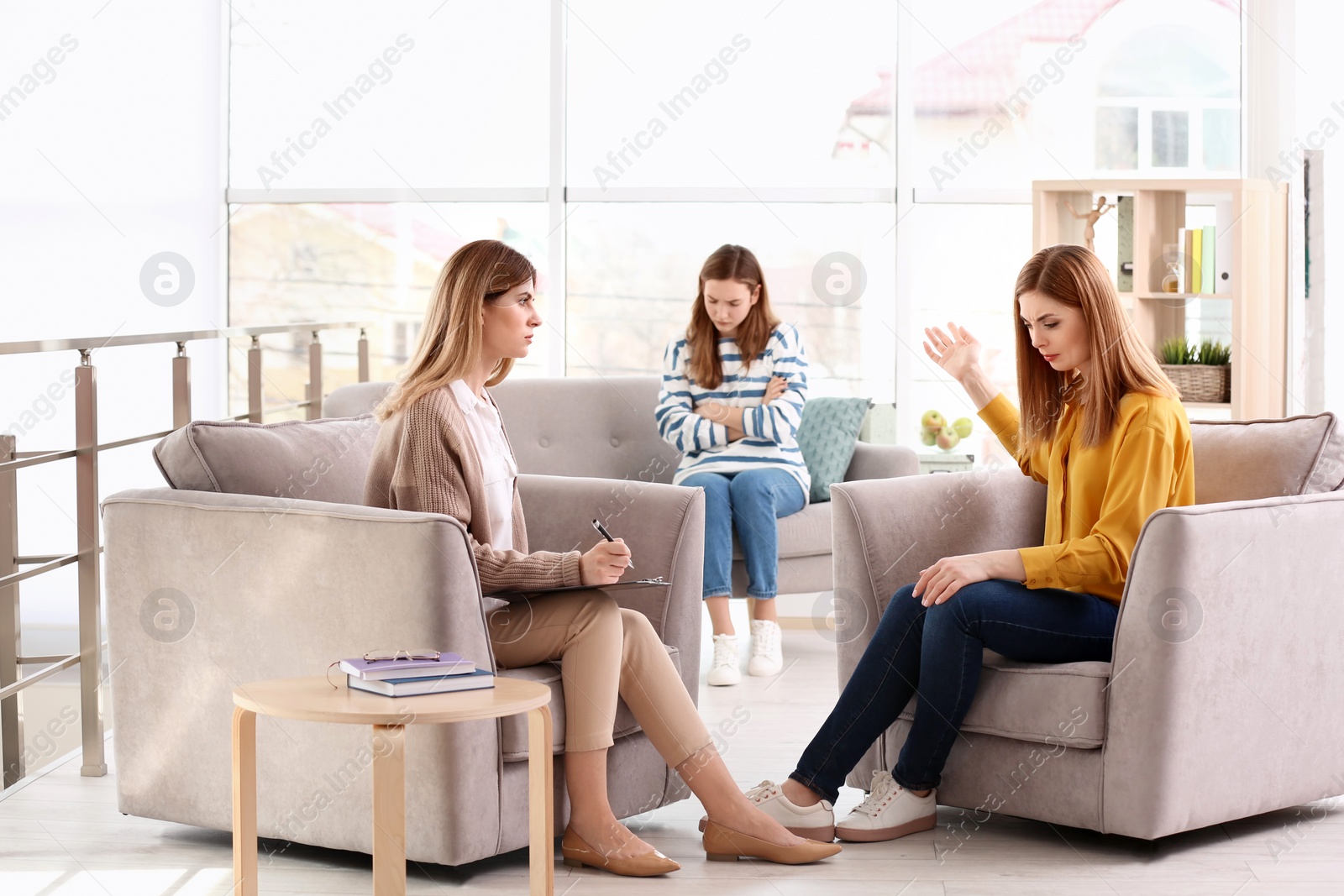 Photo of Young female psychologist working with teenage girl and her mother in office