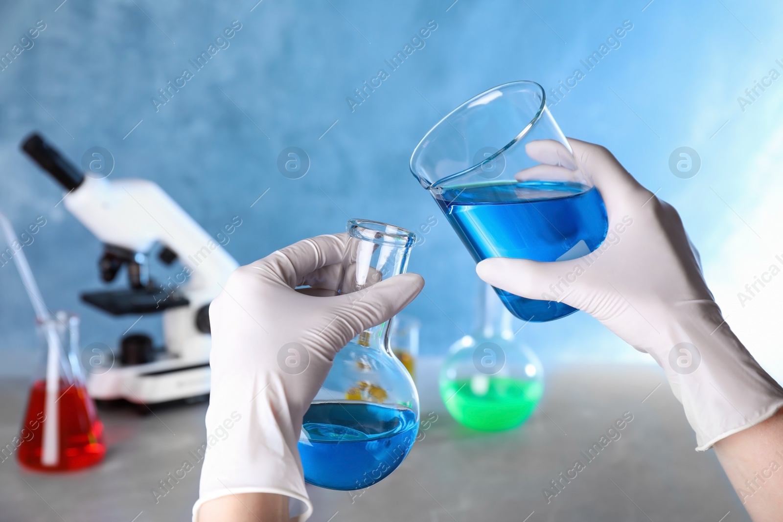 Photo of Assistant pouring sample into glass flask in chemistry laboratory, closeup