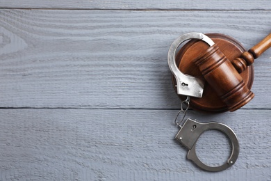 Photo of Flat lay composition with handcuffs and gavel on grey wooden table, space for text. Criminal law