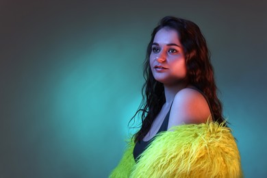 Photo of Portrait of beautiful woman in yellow fur coat on dark background with neon lights. Space for text
