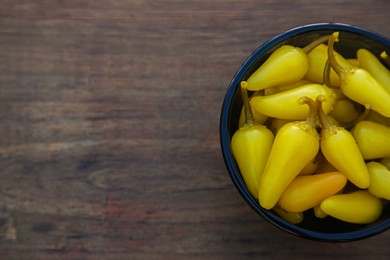 Photo of Bowl of pickled yellow jalapeno peppers on wooden table, top view. Space for text