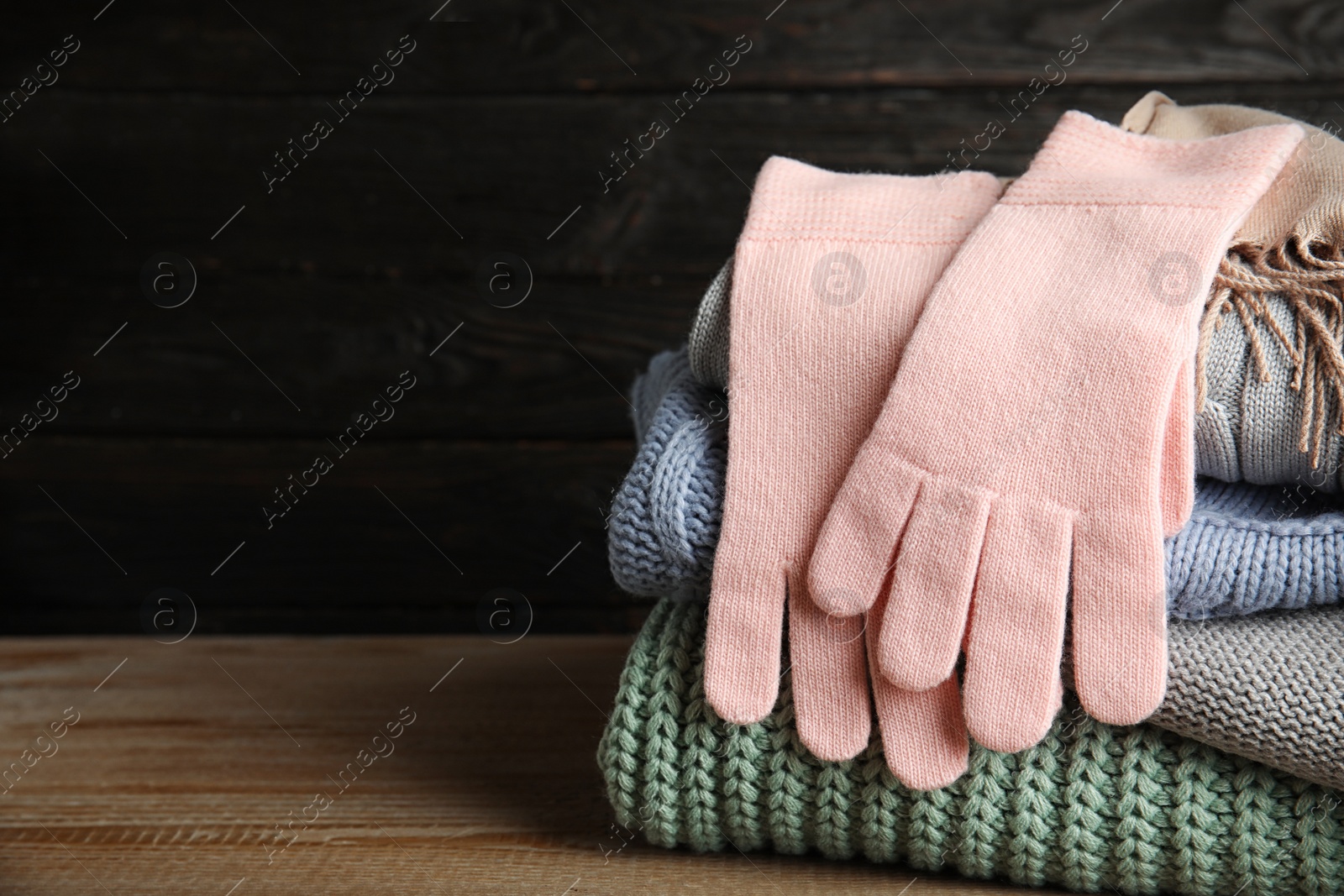 Photo of Stacked sweaters and gloves on wooden table against dark background, closeup with space for text. Autumn clothes