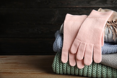 Photo of Stacked sweaters and gloves on wooden table against dark background, closeup with space for text. Autumn clothes