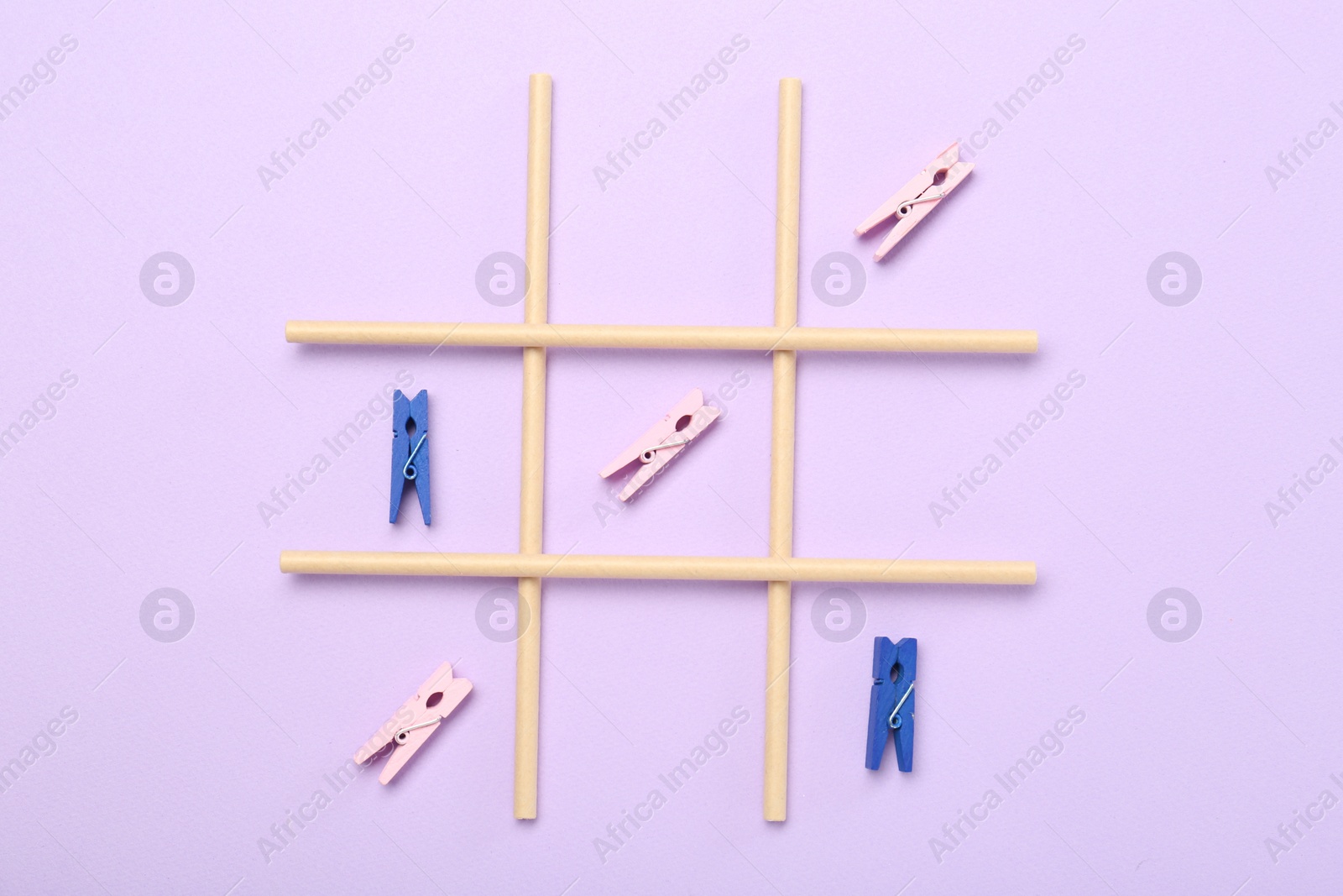 Photo of Tic tac toe game made with clothespins on violet background, top view