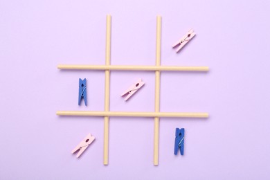 Tic tac toe game made with clothespins on violet background, top view