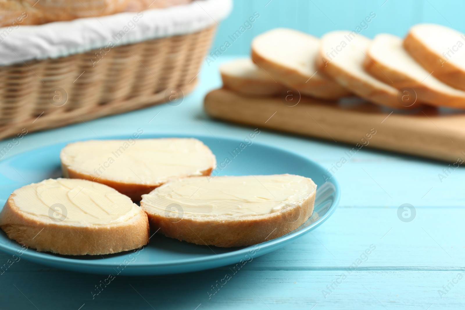 Photo of Slices of tasty fresh bread with butter on light blue wooden table