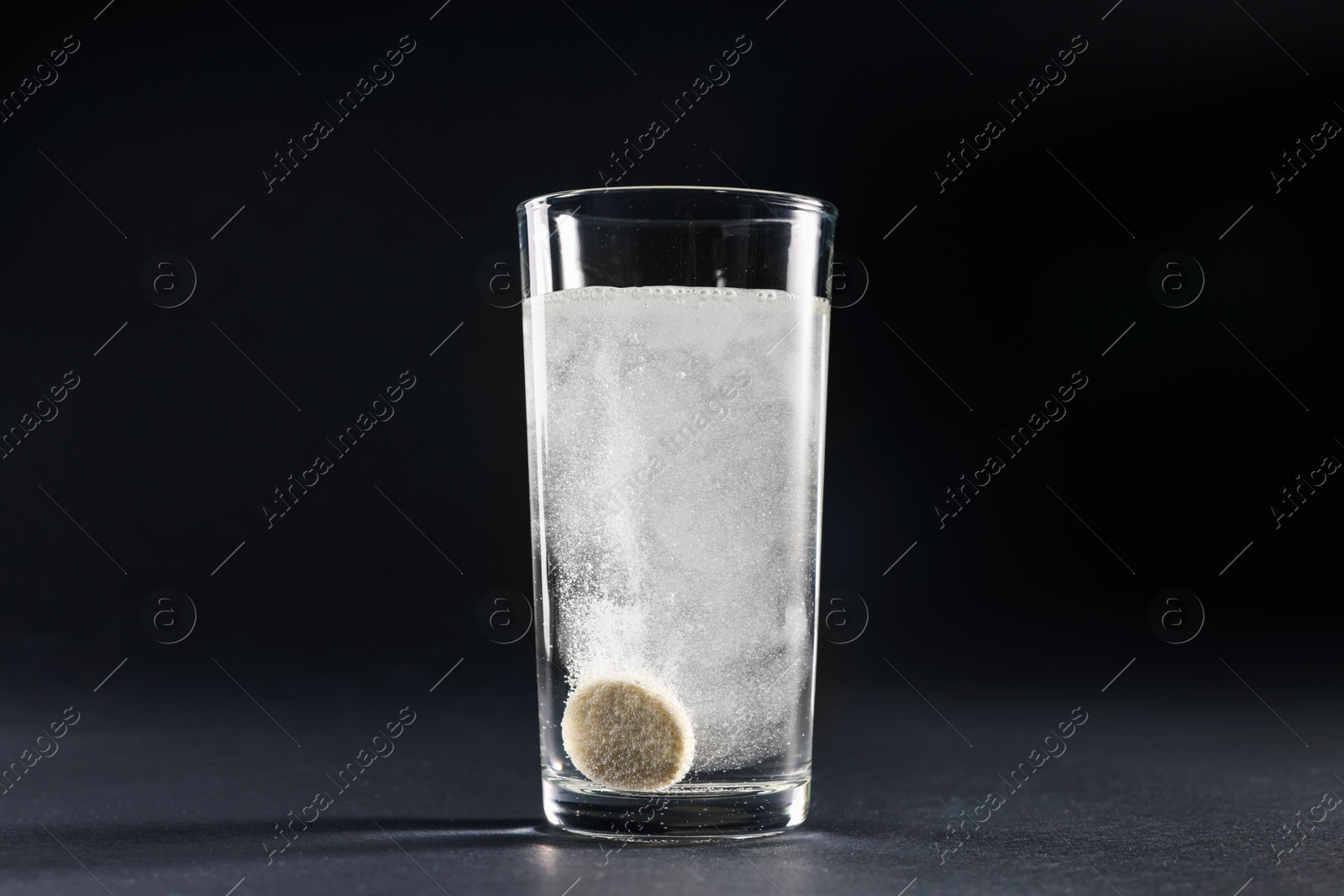 Photo of Effervescent pill dissolving in glass of water on grey table