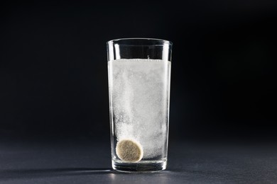 Photo of Effervescent pill dissolving in glass of water on grey table