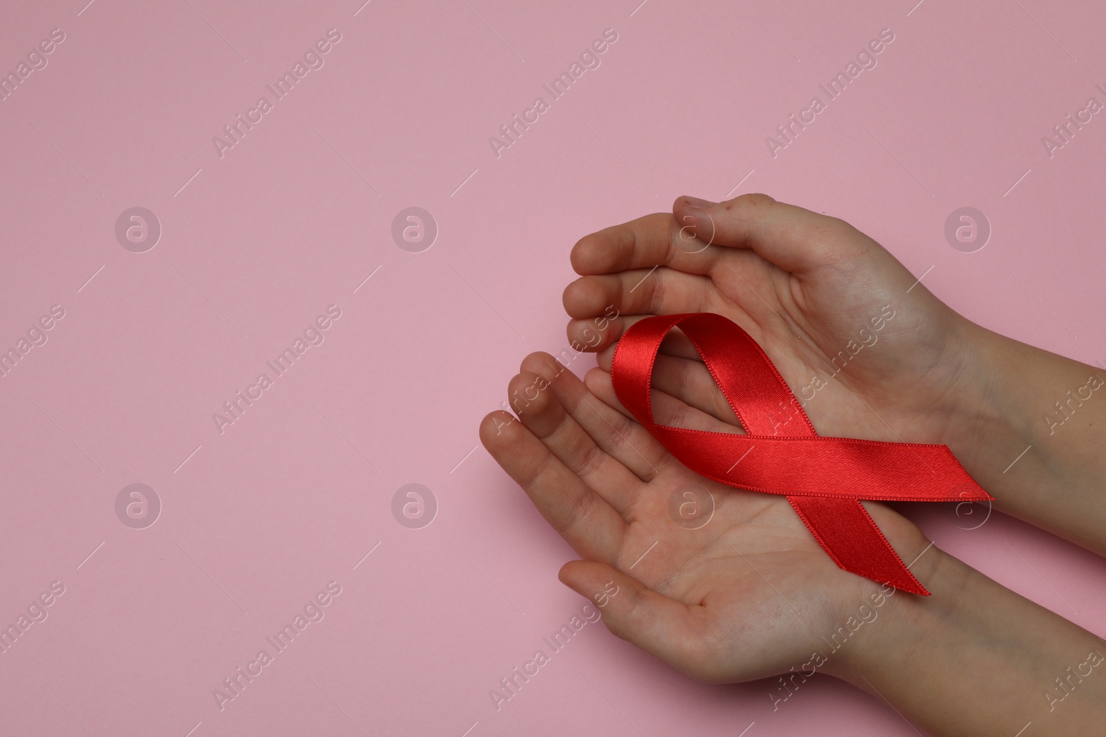 Photo of Little girl holding red ribbon on pink background, top view with space for text. AIDS disease awareness