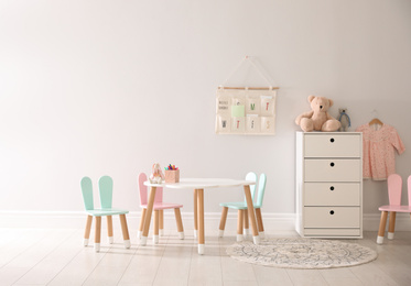 Small table and chairs with bunny ears indoors, space for text. Children's room interior