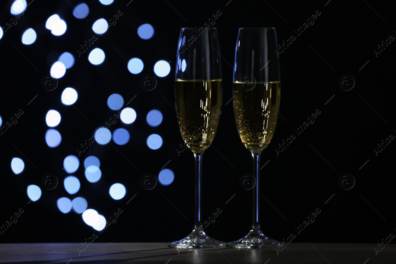 Photo of Glasses of champagne on grey table against blurred lights. Space for text