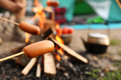 Photo of Frying sausage on bonfire outdoors. Camping season