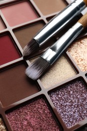 Photo of Beautiful eye shadow palette and brushes on table, closeup