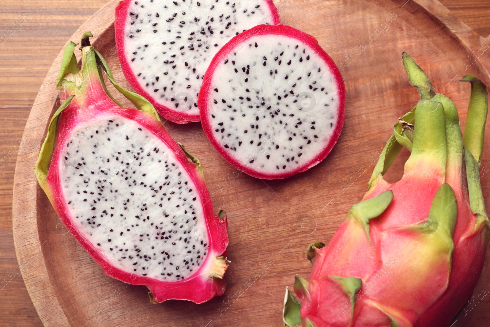 Photo of Wooden plate of delicious cut and whole white pitahaya fruits on table, top view