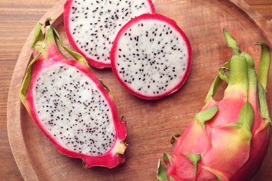 Wooden plate of delicious cut and whole white pitahaya fruits on table, top view