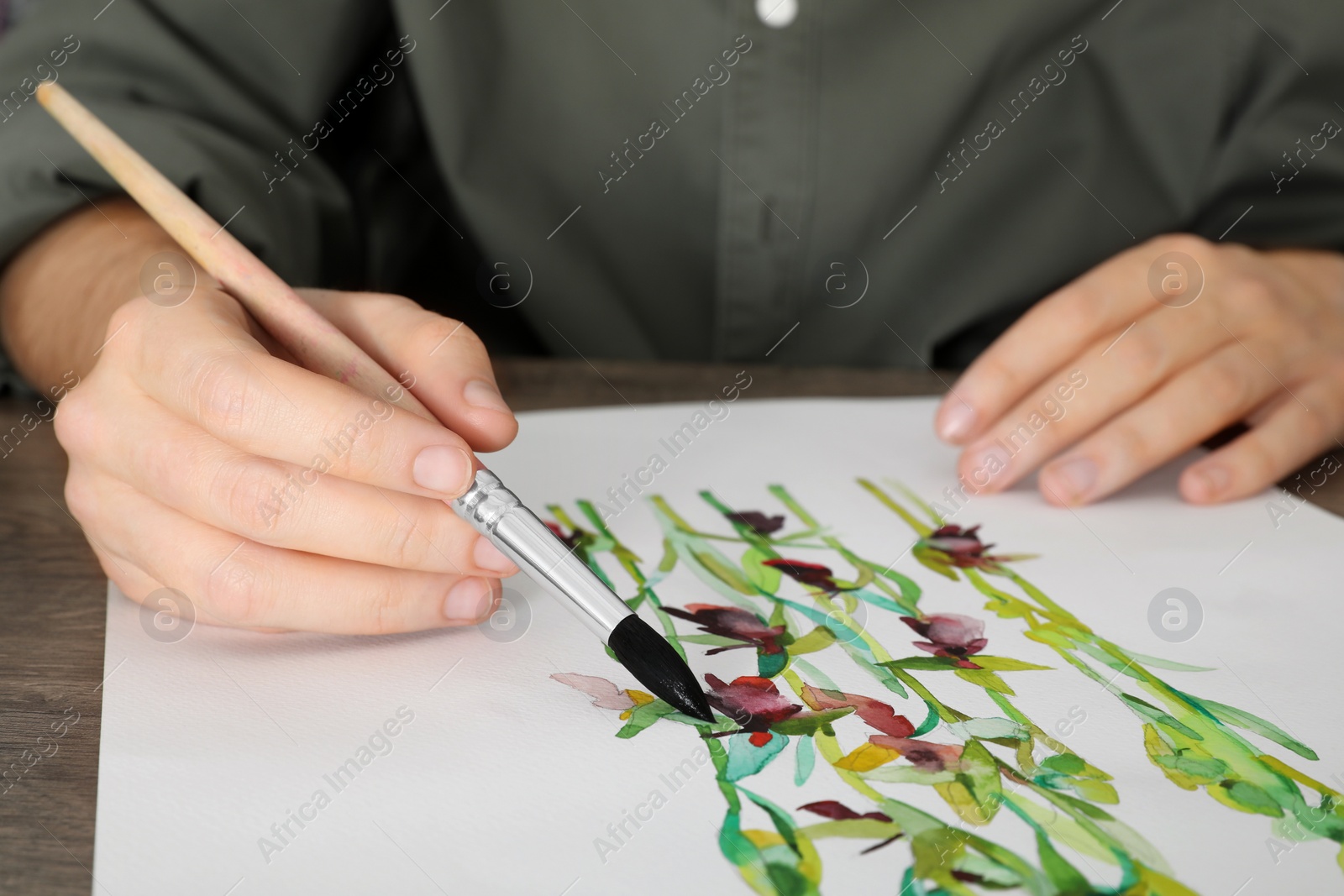 Photo of Man painting flowers with watercolor at wooden table, closeup. Creative artwork