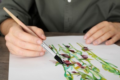 Man painting flowers with watercolor at wooden table, closeup. Creative artwork