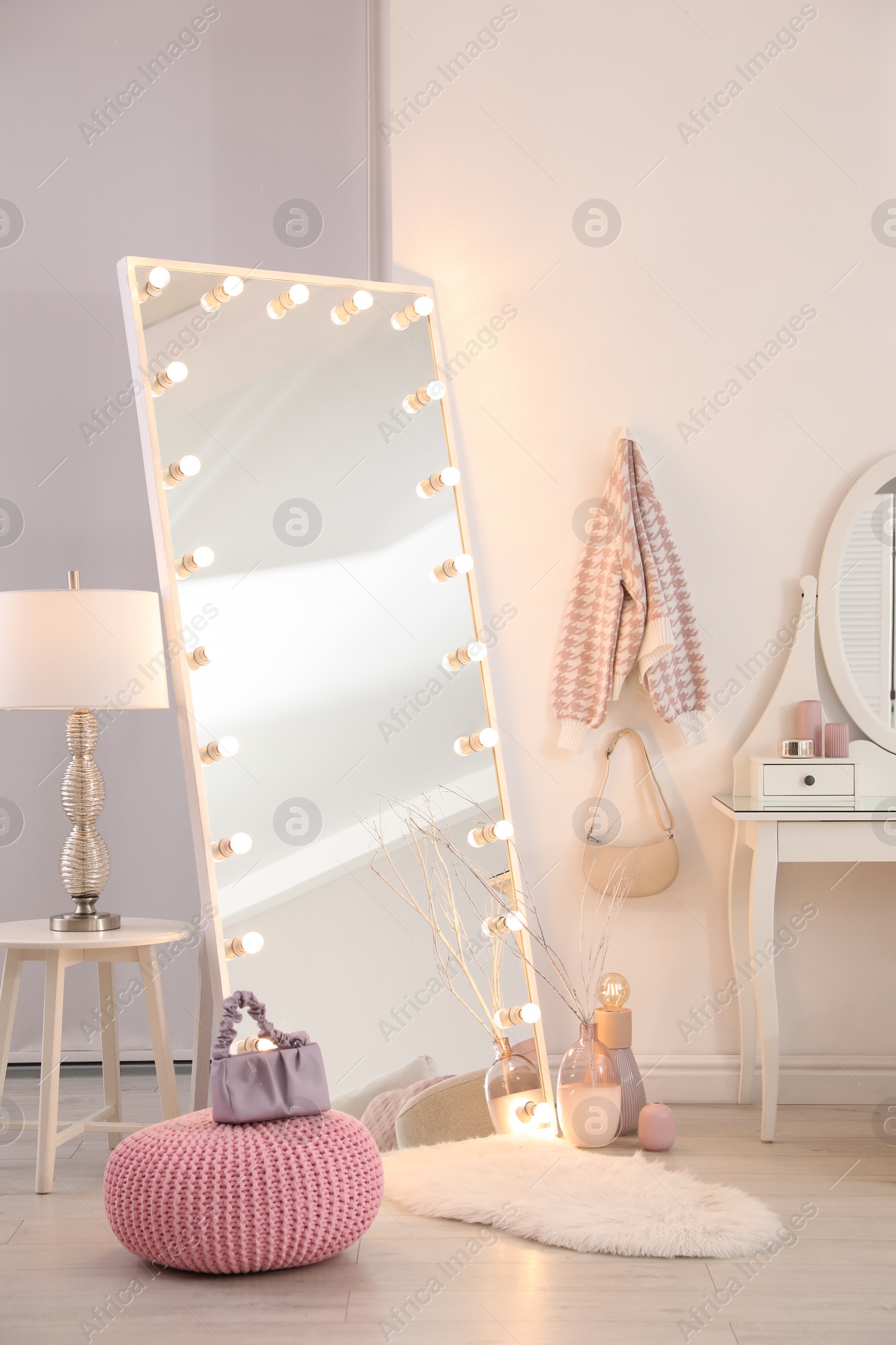 Photo of Large mirror with light bulbs and knitted pouf in stylish room. Interior design