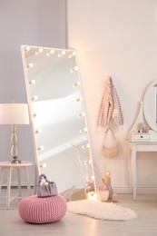 Large mirror with light bulbs and knitted pouf in stylish room. Interior design