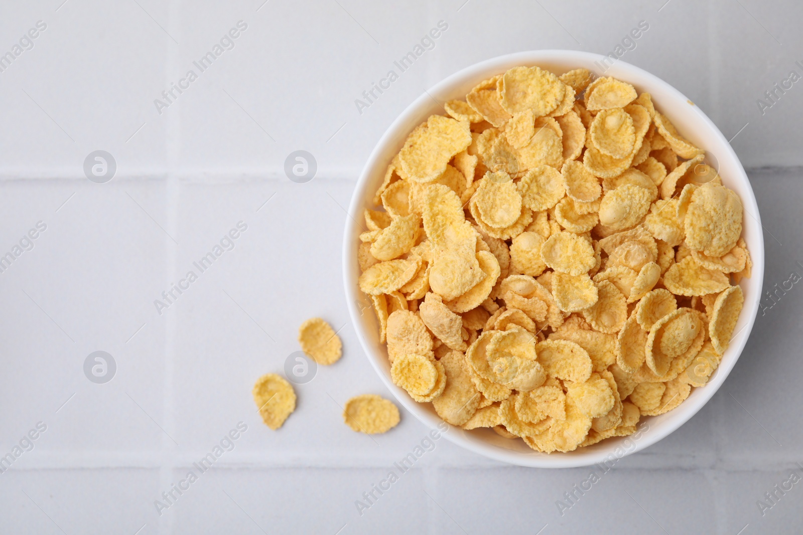 Photo of Breakfast cereal. Tasty crispy corn flakes in bowl on white tiled table, top view. Space for text