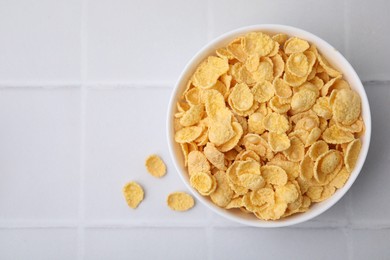 Photo of Breakfast cereal. Tasty crispy corn flakes in bowl on white tiled table, top view. Space for text