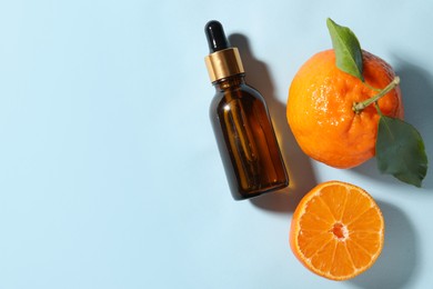 Aromatic tangerine essential oil in bottle and citrus fruits on light blue table, top view. Space for text