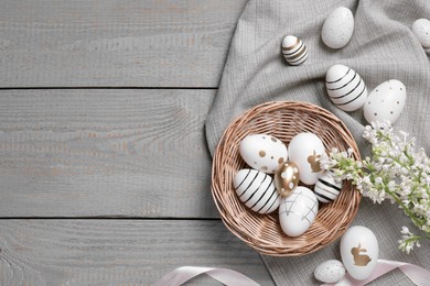 Many painted Easter eggs, branch with lilac flowers and ribbon on grey wooden table, flat lay. Space for text