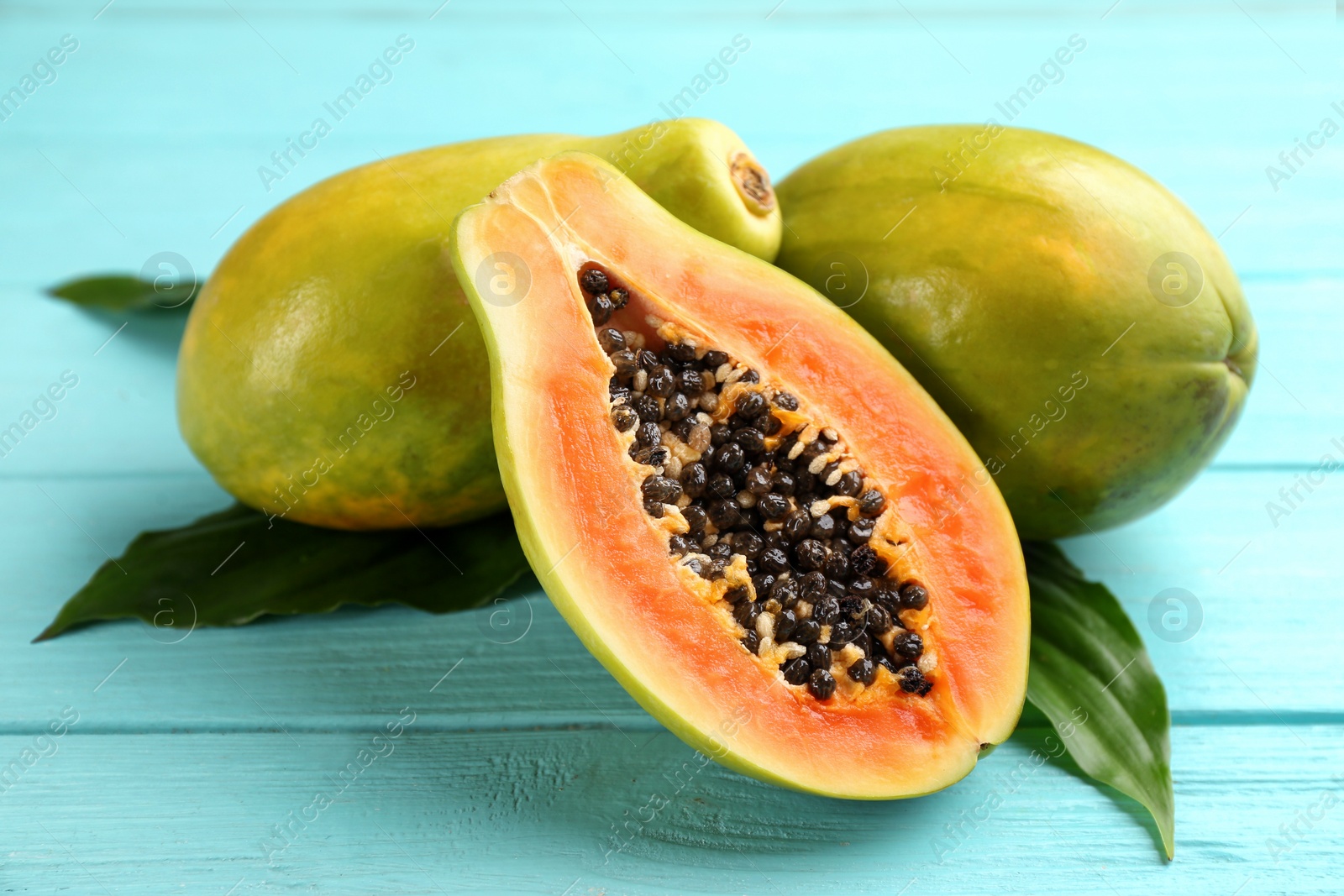 Photo of Fresh ripe papaya fruits with green leaves on turquoise wooden table