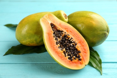 Fresh ripe papaya fruits with green leaves on turquoise wooden table