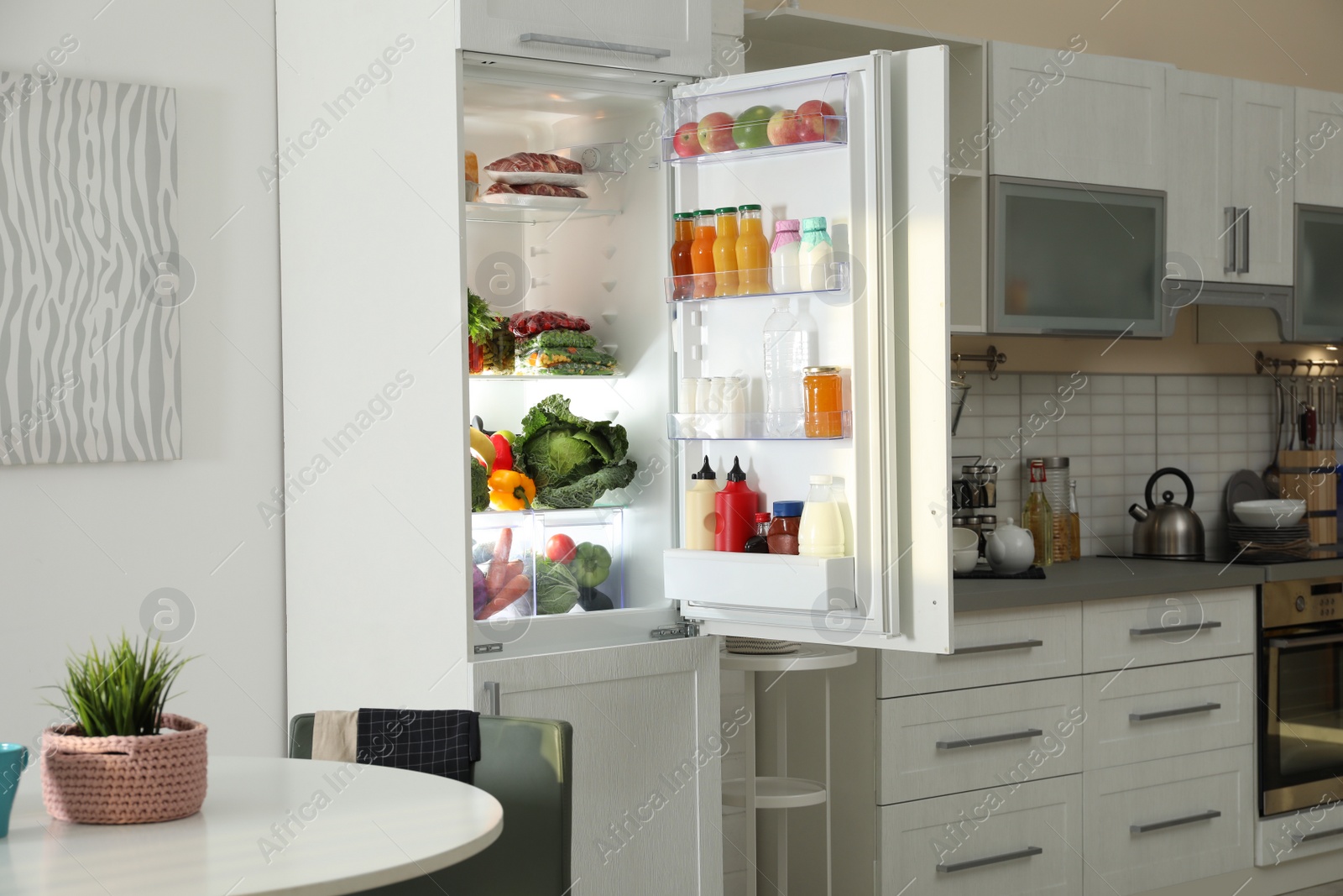 Photo of Open refrigerator full of products in stylish kitchen interior