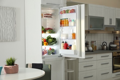 Photo of Open refrigerator full of products in stylish kitchen interior