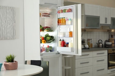 Open refrigerator full of products in stylish kitchen interior