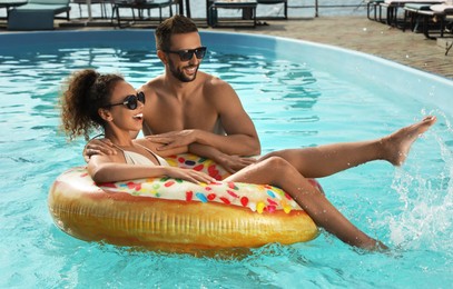 Happy couple with inflatable ring in outdoor swimming pool on sunny summer day