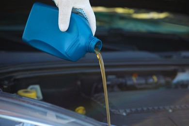 Man pouring motor oil from blue container, closeup. Space for text