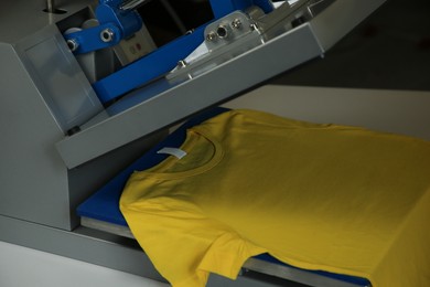 Photo of Printing logo. Heat press with yellow t-shirt on white table