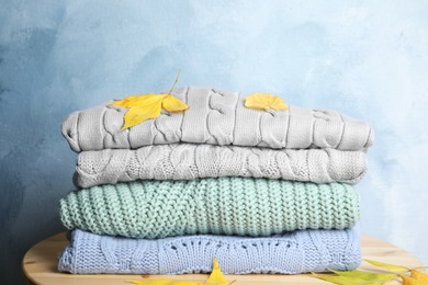 Photo of Stack of warm clothes and autumn leaves on wooden table against light blue background