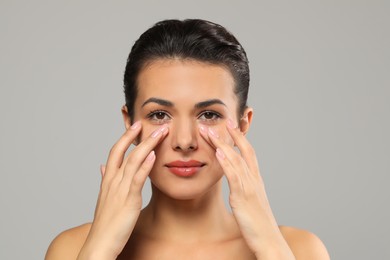 Photo of Woman applying cream under eyes on grey background. Skin care