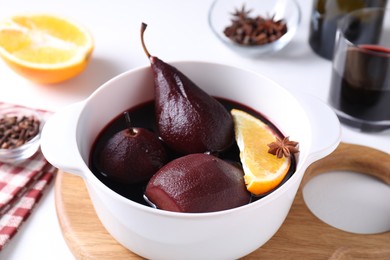 Tasty red wine poached pears in pot and orange on white table, closeup