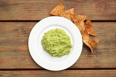 Photo of Delicious guacamole made of avocados and nachos on wooden table, flat lay