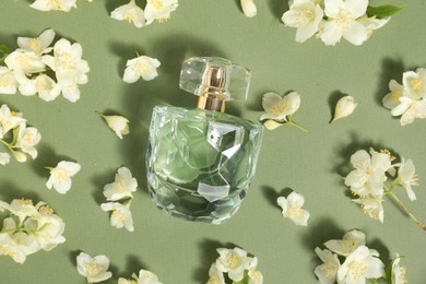 Photo of Aromatic perfume in bottle among beautiful jasmine flowers on pale green background, flat lay