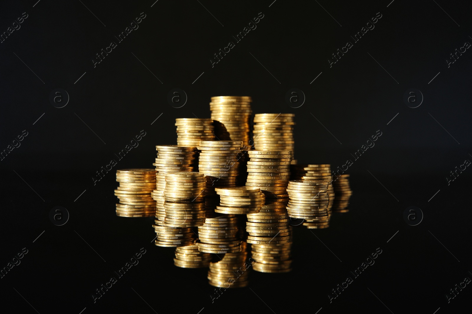 Photo of Many stacks of coins on mirror surface against black background